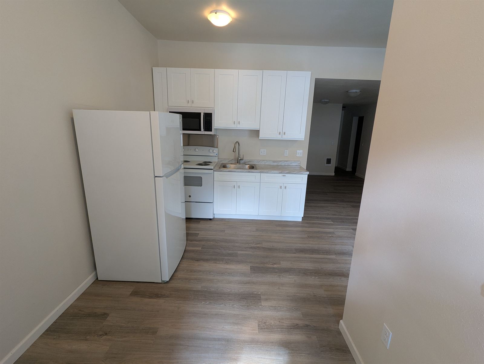 Renovated kitchen with white shaker cabinets, white appliances, and gray LVP flooring in Unit 2
